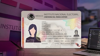 Una credencial para votar del INE de México se muestra en primer plano sobre un escritorio de madera, con un ordenador portátil y documentos borrosos al fondo.
