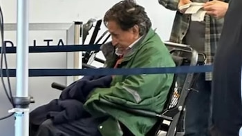 Alejandro Toledo viste una casaca verde y permanece sentado en una silla de ruedas detrás de una cinta delimitadora azul
