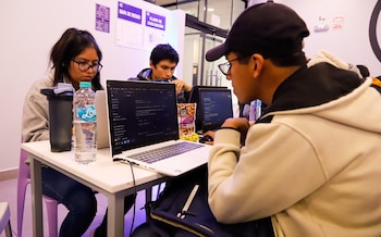 Tres jóvenes sentados ante una mesa blanca utilizan computadoras portátiles junto a botellas de agua y paquetes de alimentos