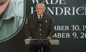 El sheriff Carl Ritchie, en uniforme oscuro y con gafas, habla detrás de un podio transparente con un micrófono