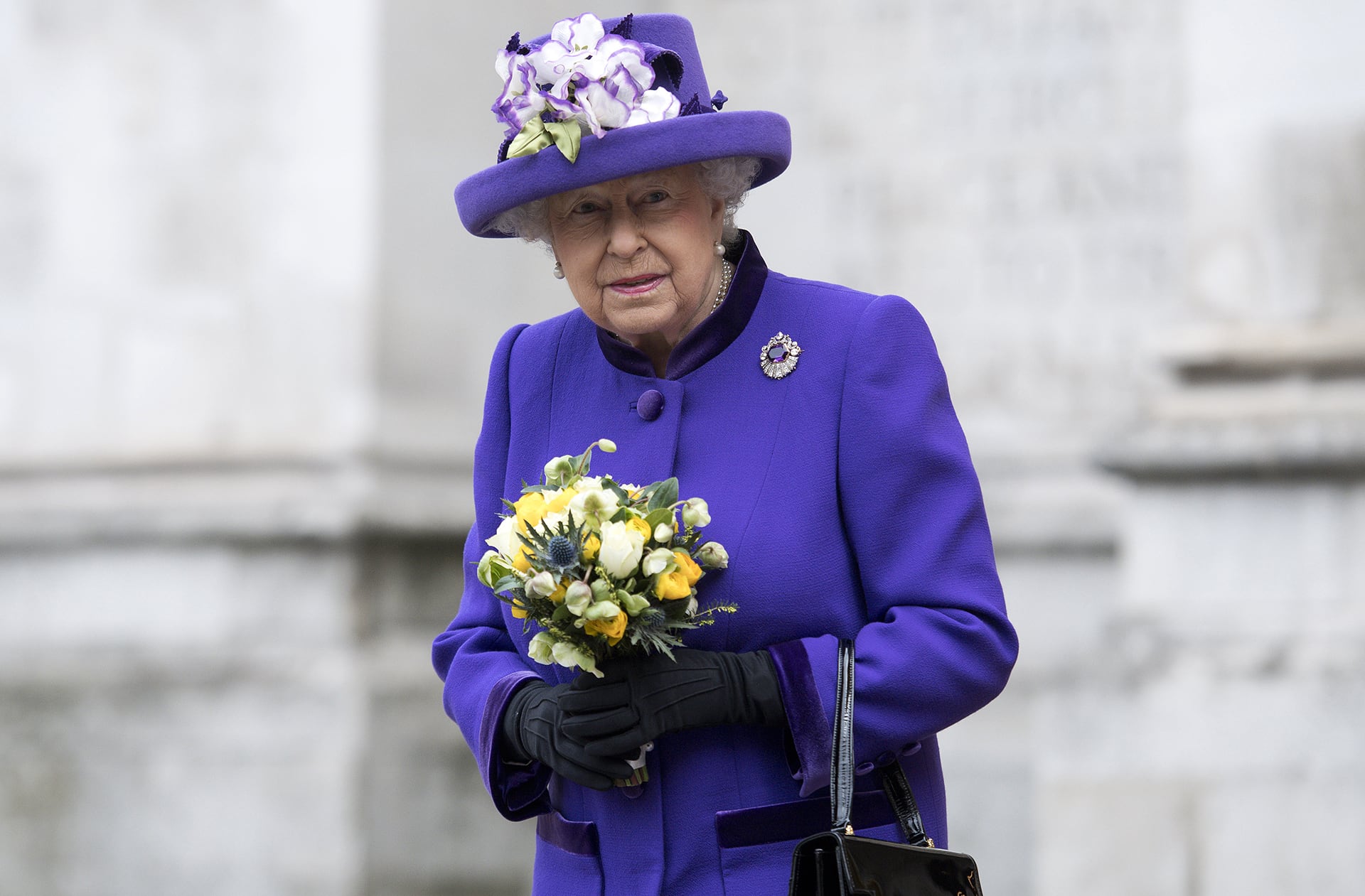 Abrigo y sombrero púrpura intenso con flores textiles blancas y violetas, broche de gema violeta y guantes negros para un evento oficial (AFP)