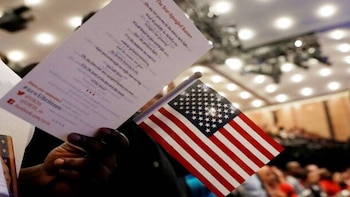 Primer plano de una mano sosteniendo una bandera pequeña de Estados Unidos y un folleto con las letras del himno nacional en un evento