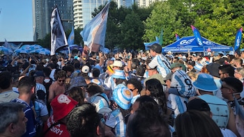 Una multitud de personas reunida al aire libre. Muchos visten camisetas y sombreros celestes y blancos. Se observan banderas argentinas y un toldo azul