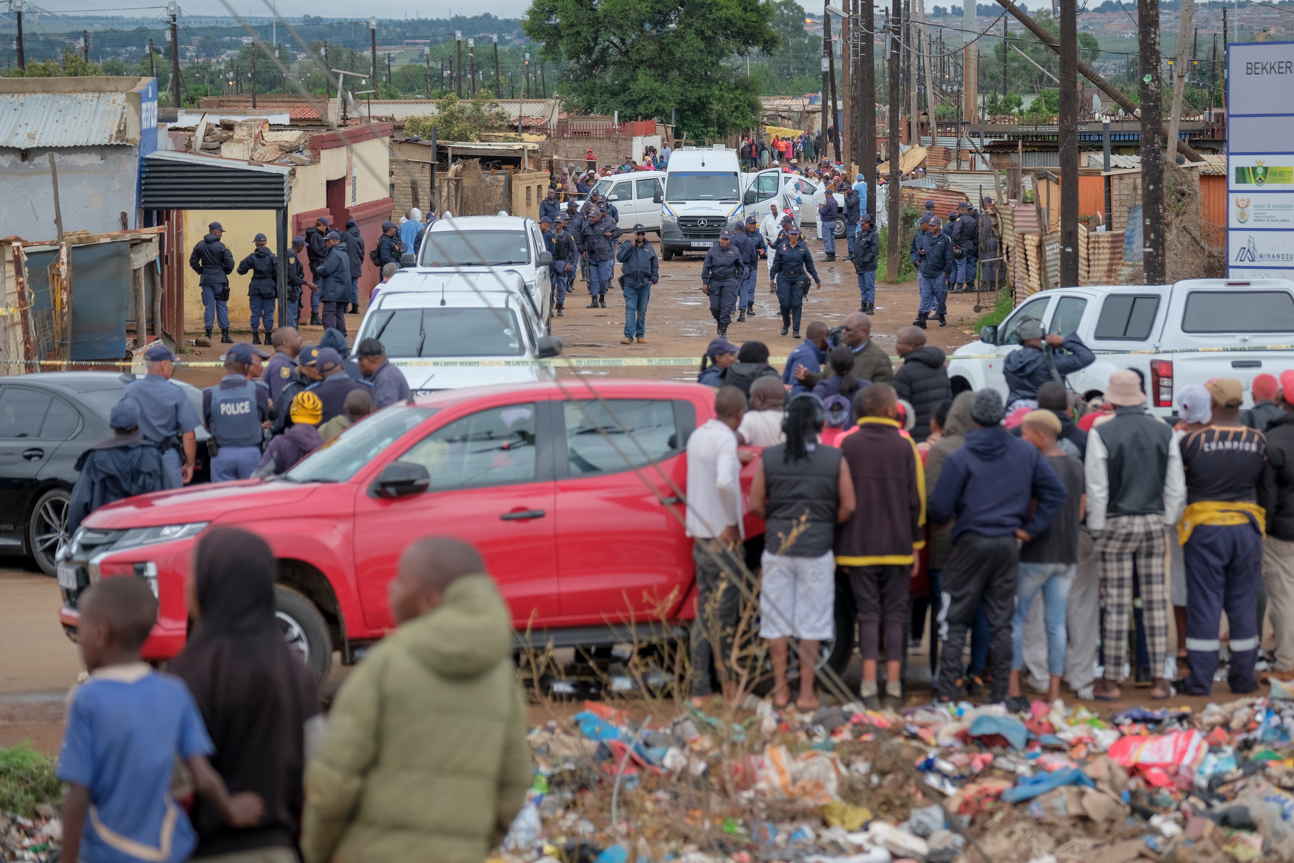 Los residentes observan cómo los oficiales del Servicio de Policía Sudafricano (SAPS) se reúnen en la escena de un ataque en una taberna en Bekkersdal (Emmanuel Croset/AFP)