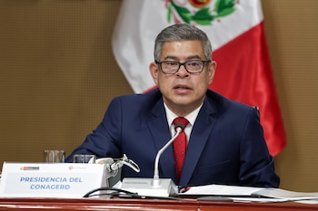 Luis Galarreta con traje azul, corbata roja y anteojos, sentado frente a un micrófono y un cartel con el texto Presidencia del CONAGERD