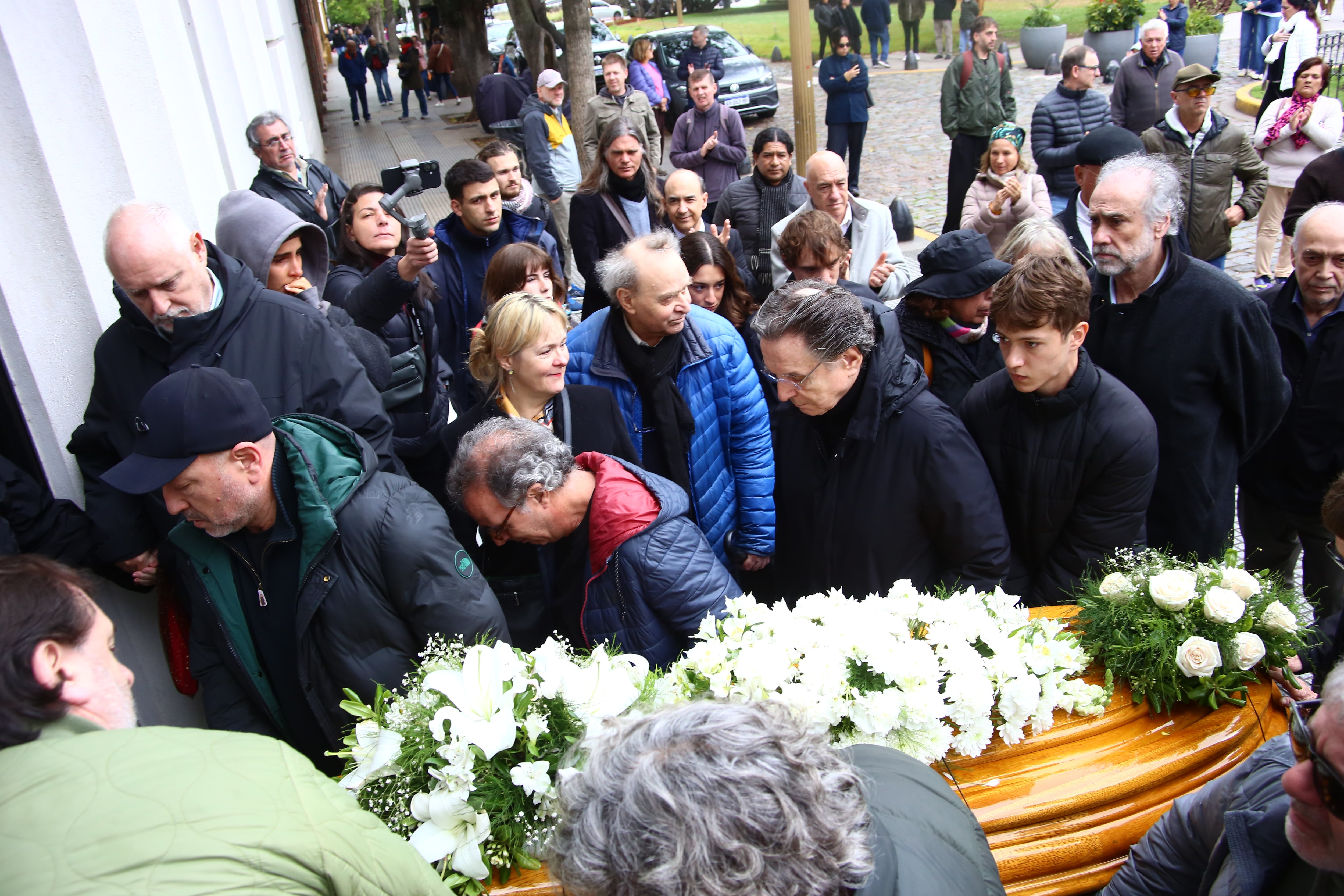 Allegados y seguidores acompañan el féretro cubierto de flores blancas durante la despedida del cantante Piero en el Cementerio de la Recoleta, entre los que se encuentran Ámbar de Benedictis, Gustavo Luteral y su esposa Mariana Schettini
