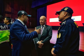 Tres hombres conversan. Uno con traje y gorra de Guatemala, otro con traje, y el tercero con uniforme policial y gorra de tránsito