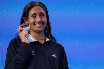 Mujer sonriente de cabello mojado con chaqueta deportiva azul marino, sujetando medalla de bronce con inscripción Pan Pacific y 2025 sobre fondo azul