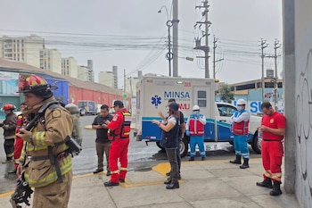 Bomberos vestidos con trajes de protección y personal de salud junto a una ambulancia en una esquina urbana