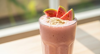 Licuado cremoso y rosado de guayaba y avena en vaso alto, decorado con rodajas de guayaba y avena espolvoreada, con un fondo luminoso y natural.