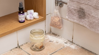 Un baño con un frasco de aceite esencial, bolas de algodón, una bolsa con virutas, una toalla, un frasco con pececillos de plata y pan, y polvo blanco en el suelo.