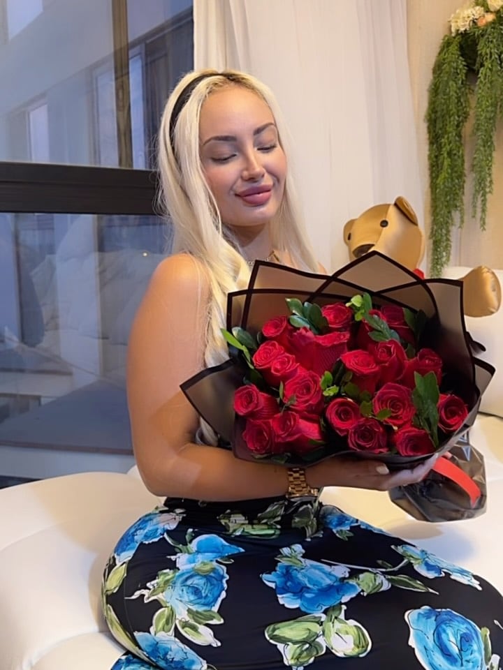 La modelo Nadeska Widausky, recientemente capturada por la Interpol, sonríe con los ojos cerrados mientras posa con un gran ramo de rosas rojas envueltas en papel oscuro.