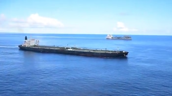 Vista aérea de un gran petrolero oscuro en el primer plano y otro buque al fondo, navegando en el vasto océano azul bajo un cielo con nubes