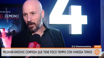 Un hombre calvo y con barba habla frente a un micrófono rojo que lleva el logotipo de un canal de televisión
