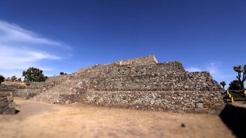 Estructura de piedra escalonada, cielo azul con nubes, terreno seco y vegetación dispersa