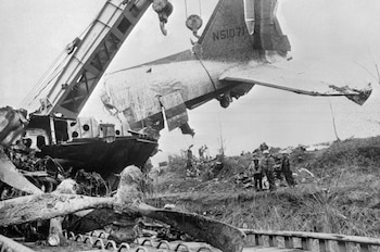 Una grúa levanta la sección de cola de un avión con matrícula N51071. Escombros, una hélice grande y varias personas en terreno abierto. Foto en blanco y negro
