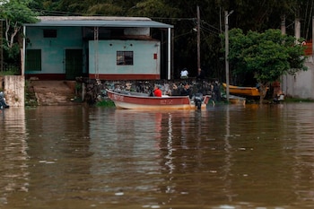 Un bote con ocupantes navega sobre agua turbia frente a una vivienda y árboles en un área inundada