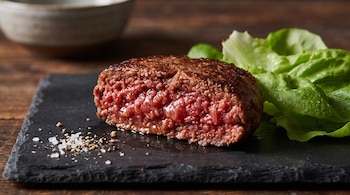 Una hamburguesa vegetal cortada a la mitad, lechuga verde y granos de sal sobre una tabla de pizarra negra.