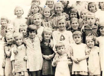 Fotografía en blanco y negro de un grupo de aproximadamente veinte niños de diversas edades, algunos con marcas en forma de "X" en sus cabezas