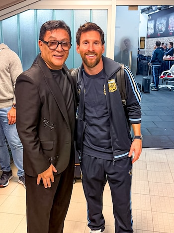 Lionel Messi con indumentaria de la selección argentina y Sergio Torres con saco negro y gafas posan de pie en un espacio interior