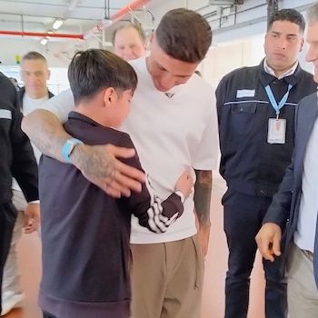 Enzo Fernández viste una camiseta blanca y abraza a un niño con chaqueta negra en un pasillo rodeados de otras personas