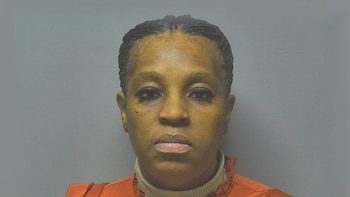 Foto policial de una mujer afroamericana con trenzas, mirando directamente a la cámara, vistiendo una prenda naranja sobre un cuello alto claro