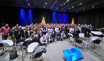 Un grupo de personas posa en un salón de eventos con sillas blancas y negras cerca de una pantalla azul