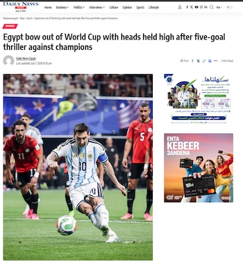 Un jugador de fútbol, Lionel Messi, patea un balón blanco y azul en un campo de césped verde. Hay otros jugadores con camisetas rojas en el fondo