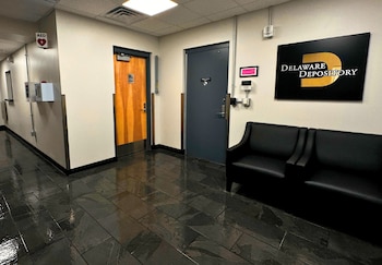 Pasillo interior con suelo de baldosas oscuras, dos sillones negros, dos puertas y un letrero con el nombre Delaware Depository