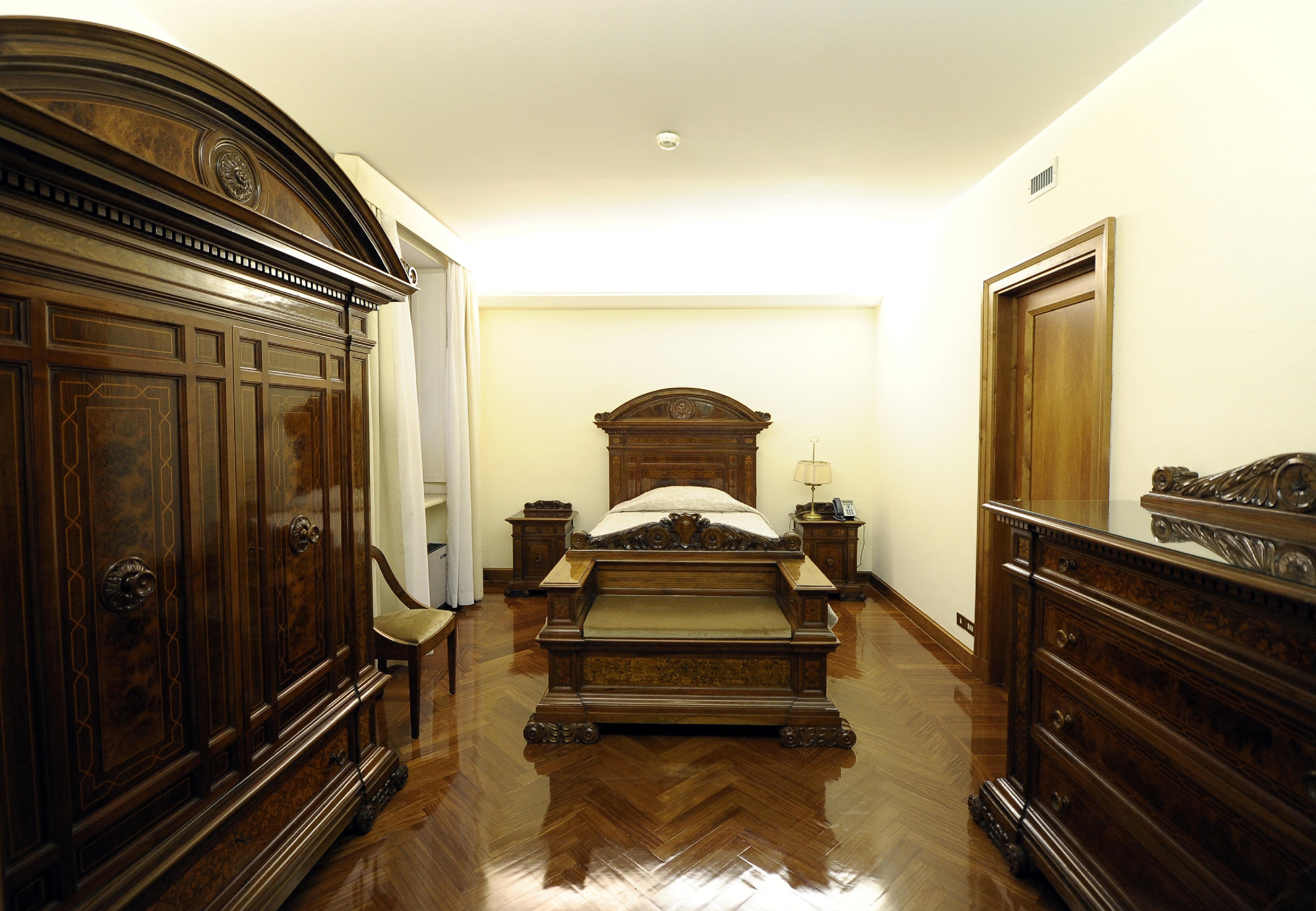 Una de las habitaciones de Santa Marta, similar a la que usa el Papa. En la propia tiene una cama individual de madera, una silla y un perchero. Hay un baño con ducha y un espejo de madera blanca
