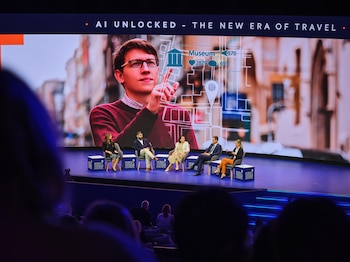 Cinco personas sentadas en un escenario durante un panel, bajo una gran pantalla con la imagen de un hombre utilizando una interfaz digital