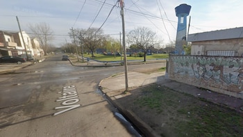 Calle Voltaire en un barrio con edificios, un parque, un tanque de agua elevado pintado y un muro de ladrillos con grafitis, bajo un cielo claro