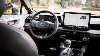 Interior de un Toyota RAV4 con volante multifunción negro y rojo, pantalla táctil central, panel de instrumentos digital y consola con palanca de cambios