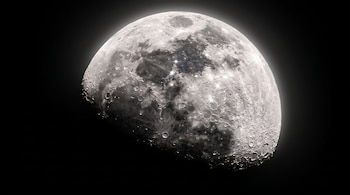 Luna en fase de cuarto creciente con múltiples cráteres y mares, iluminada y con destellos de luz plateados contra un fondo negro.
