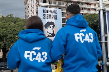 Vista trasera de dos personas con sudaderas azules 'FC43' observando una pancarta de Franco Colapinto con el lema 'Con Franco Siempre' en Buenos Aires