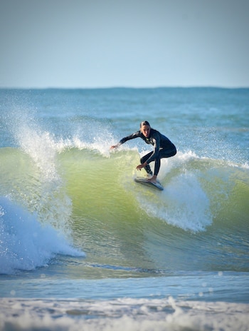Una persona con traje de neopreno negro se desliza sobre una ola con una tabla de surf en el mar