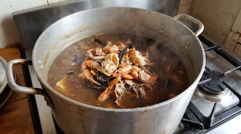 Una olla grande metálica sobre una cocina de gas contiene un caldo caliente con cáscaras de cangrejos y camarones.