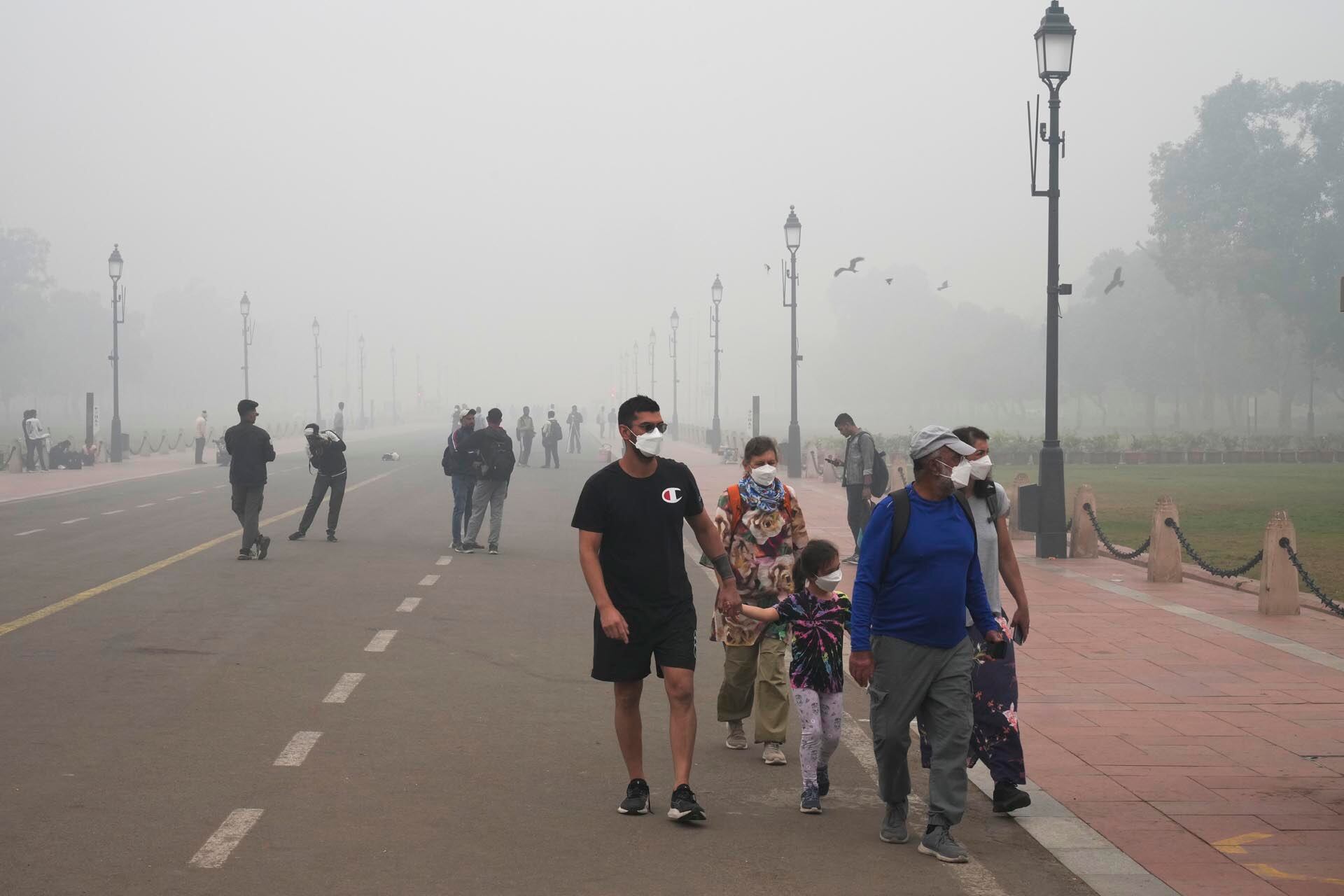 Una familia de turistas extranjeros camina con mascarillas en medio de una densa capa de smog mientras la contaminación del aire se dispara en Nueva Delhi, India, el lunes 18 de noviembre de 2024. (Foto AP/Manish Swarup)