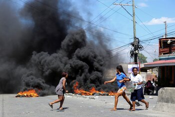 Mujeres corren junto a las barricadas callejeras en llamas en el barrio de Delmas mientras los residentes protestan por la falta de seguridad y piden ayuda al gobierno, en Puerto Príncipe, Haití, el 20 de febrero de 2025 (REUTERS/Jean Feguens Regala)
