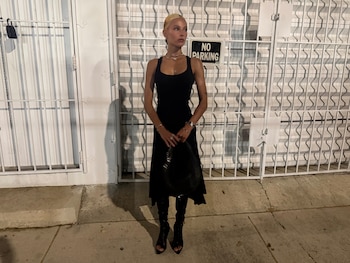 Valentina Zenere posa de noche ante una reja blanca con un cartel de prohibido estacionar, vestida con un vestido y botas negras