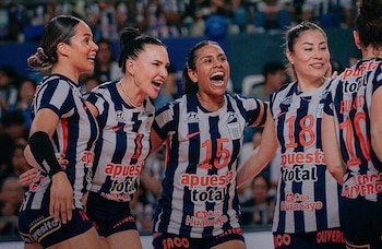 Cinco jugadoras de voleibol con camisetas de rayas azules y blancas sonríen y se abrazan en una cancha