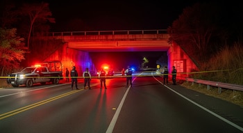 Carretera federal mexicana de noche bajo un puente de hormigón. Camioneta de Guardia Nacional, agentes con chalecos, cinta amarilla, luces policiales rojas y azules.