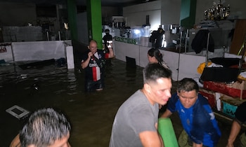 Interior de una oficina policial inundada con agua hasta las rodillas, donde varias personas evacuan objetos y se observa mobiliario sumergido