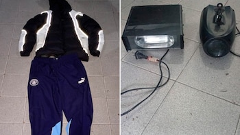 Una campera negra y blanca, un pantalón deportivo azul con logotipos, un foco de luz rectangular y una lámpara negra ovalada sobre un piso de baldosas