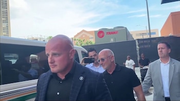 Jeff Bezos sonríe y levanta la mano derecha frente a las escaleras y puertas de vidrio de un edificio