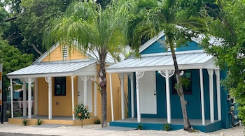 Dos casas, una amarilla y otra azul, con porches blancos y techos metálicos. Palmeras, plantas verdes y números 3501 y 3503 en las columnas.