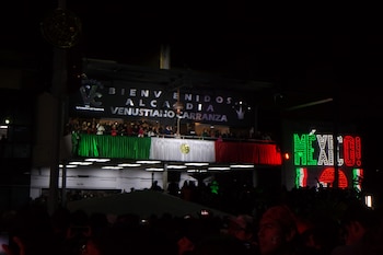 Fachada del edificio de la alcaldía Venustiano Carranza decorada con la bandera mexicana y un letrero luminoso con la palabra México de noche