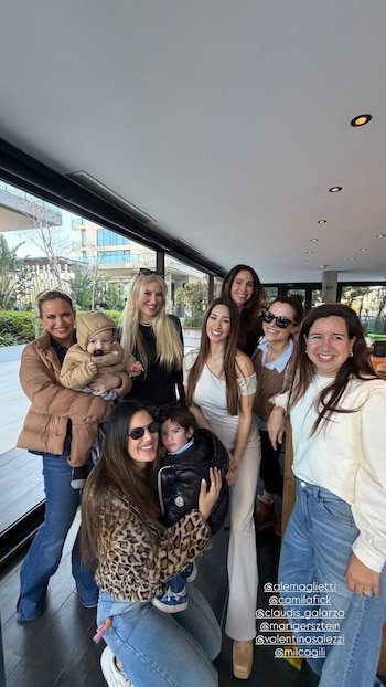 Un grupo de siete mujeres y dos niños pequeños posan sonrientes en el interior de un inmueble junto a un gran ventanal