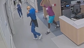 Cámara de seguridad que captura a un hombre levantando los brazos para golpear a una enfermera en el pasillo de un centro médico