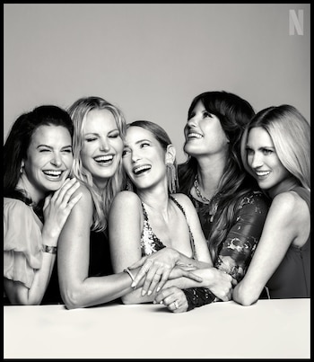 Cinco mujeres sonrientes, con expresiones de alegría, posan juntas en una fotografía en blanco y negro, apoyadas sobre una superficie clara